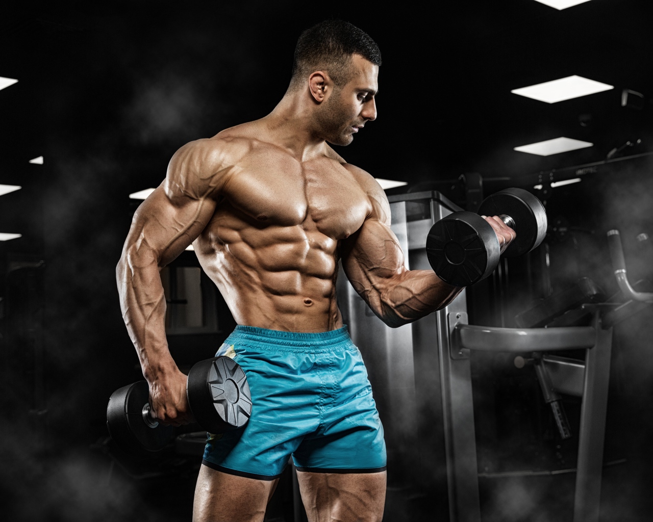 Сильный накаченный мужчина в шортах с гантелями в руках 