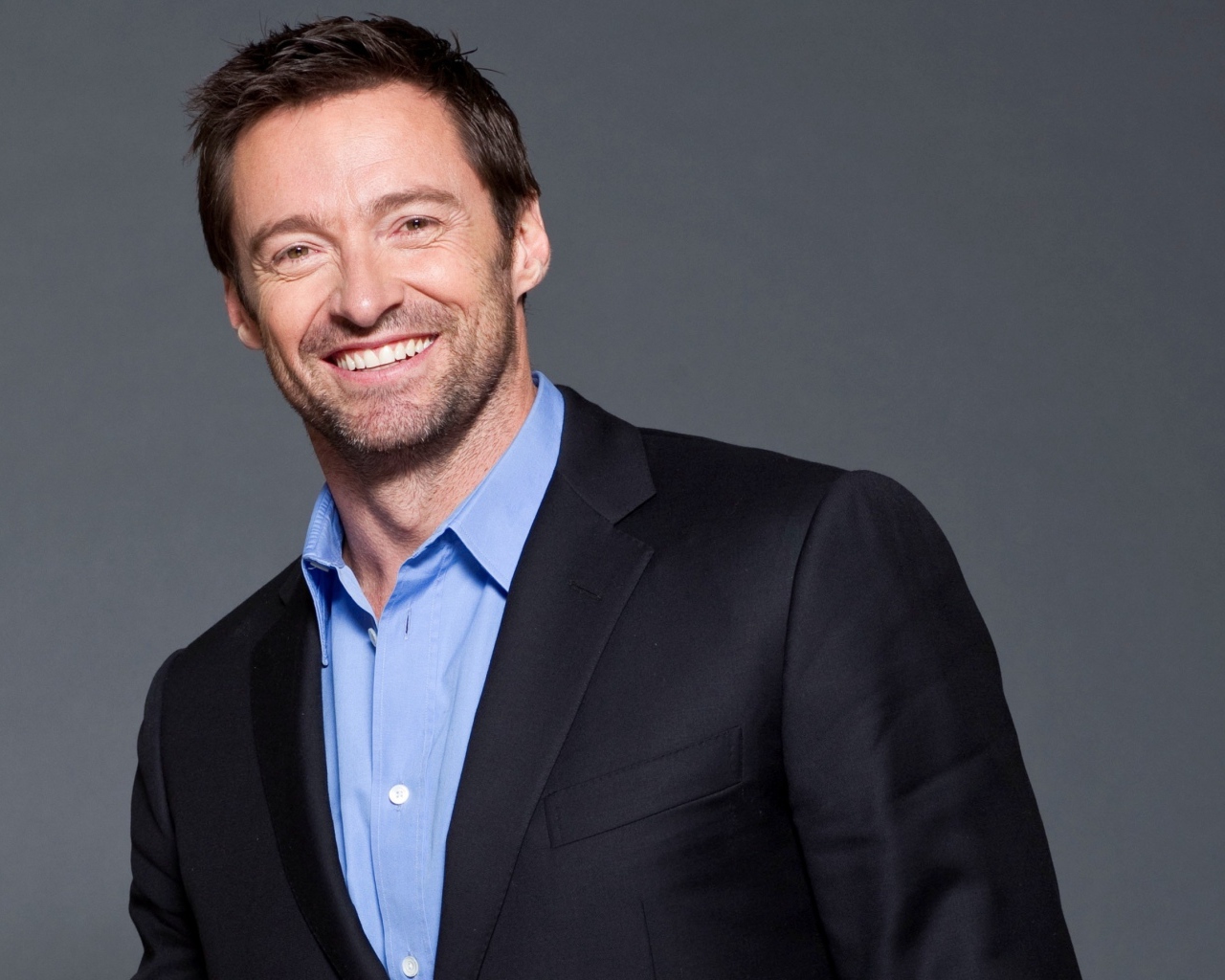 Улыбающийся мужчина, актер Хью Джекман  в костюме на сером фоне