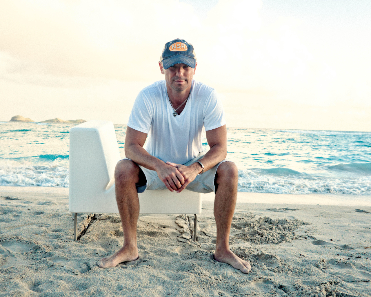 Исполнитель кантри Кенни Чесни на белом кресле на пляже