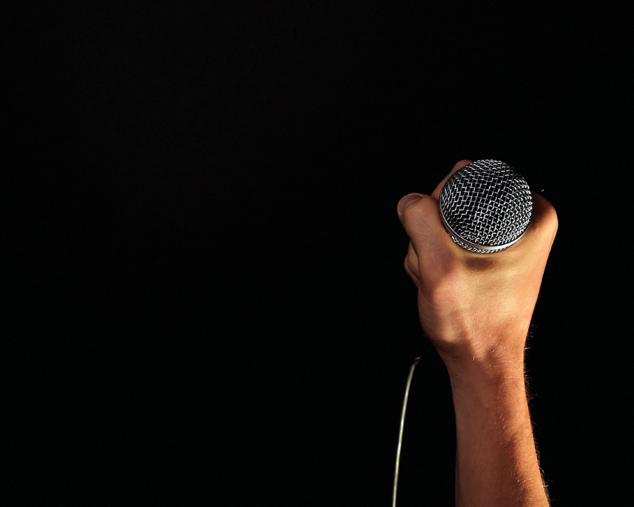 Микрофон в мужской руке на черном фоне