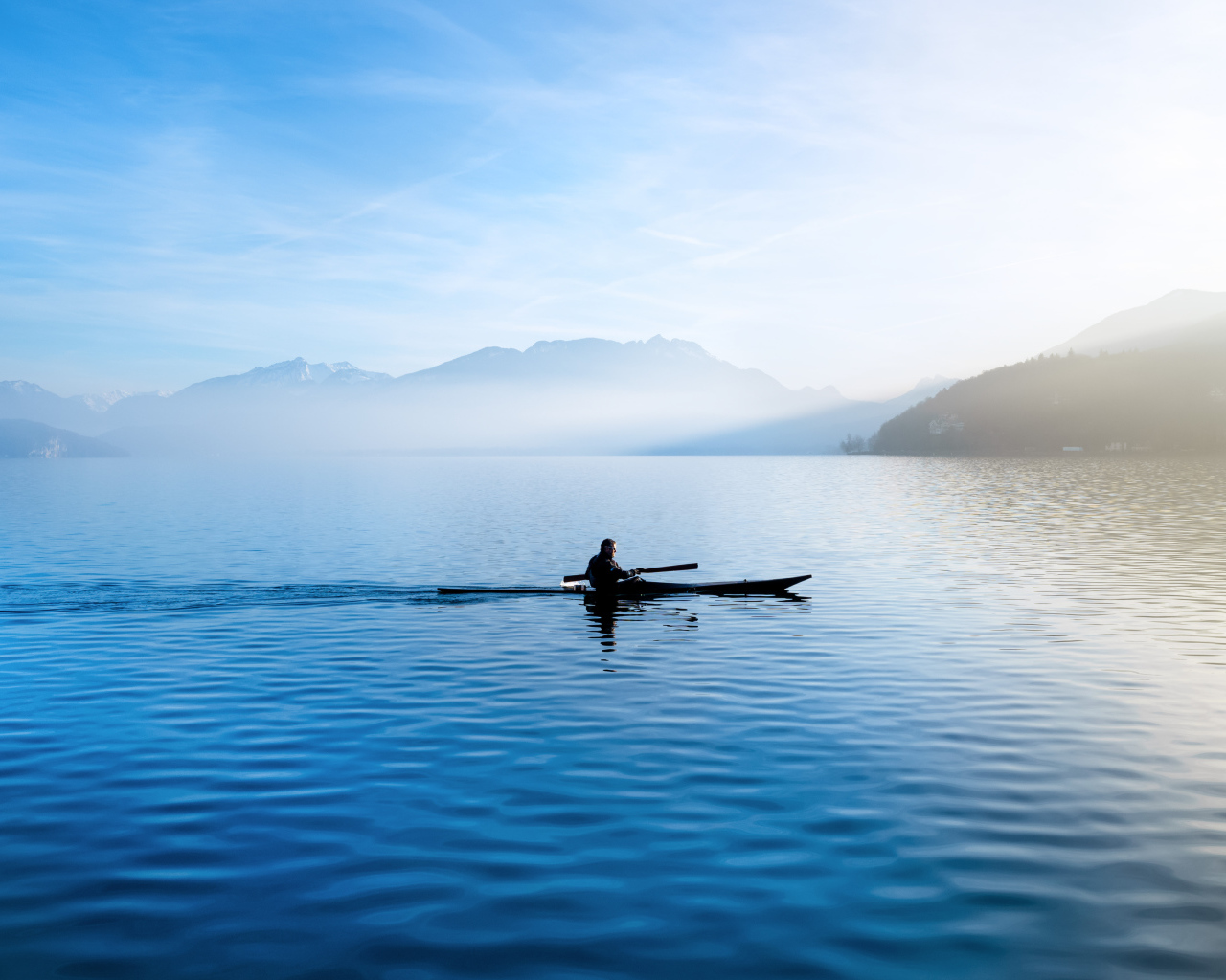 Мужчина плывет на лодке на фоне гор