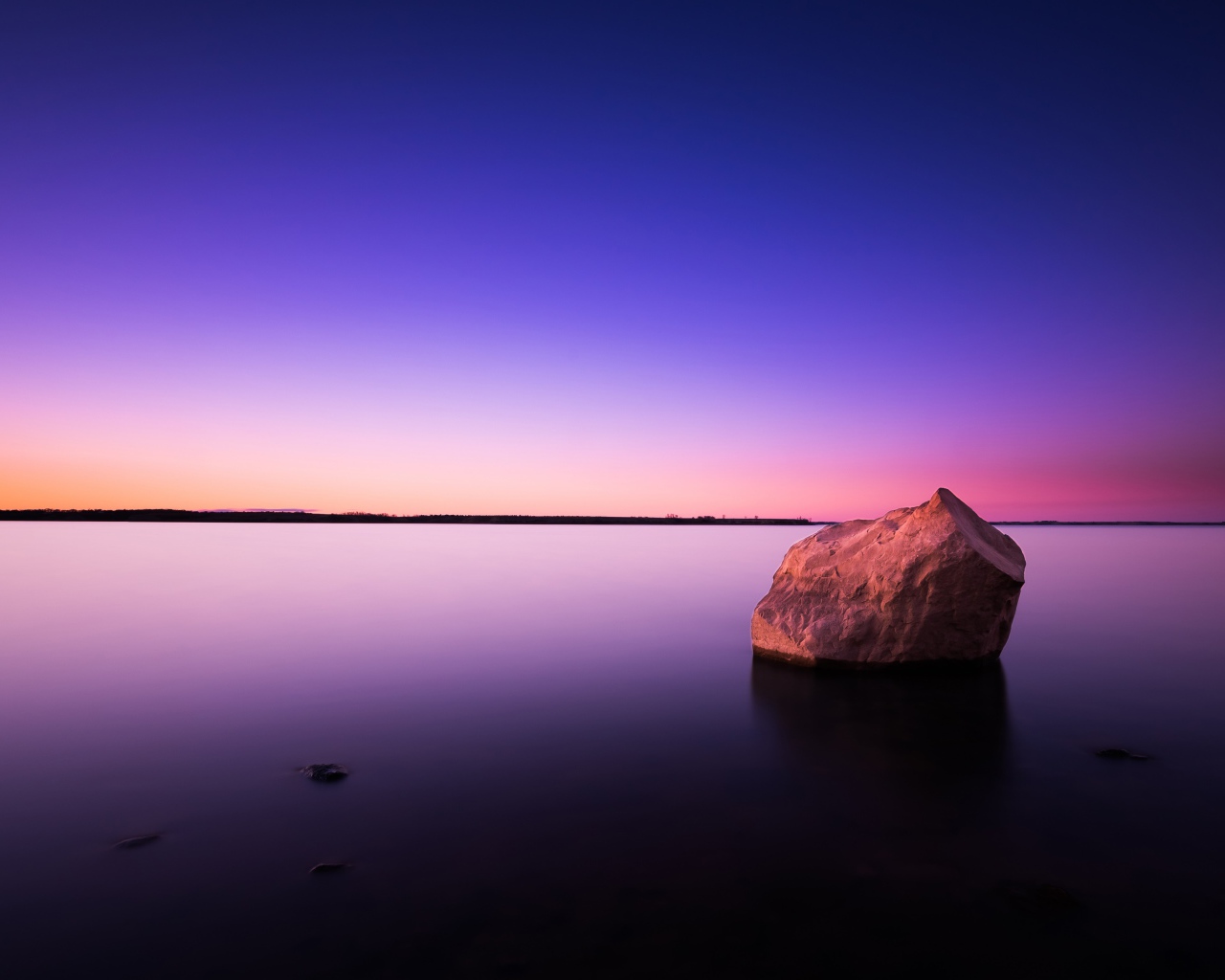 Big stone in calm water at dusk