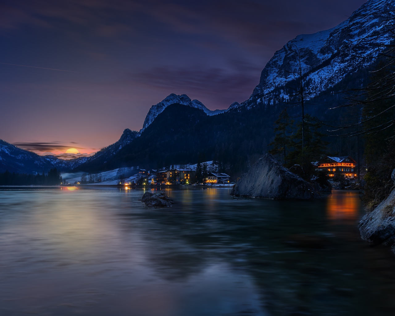 Город у озера на фоне заснеженных гор ночью 