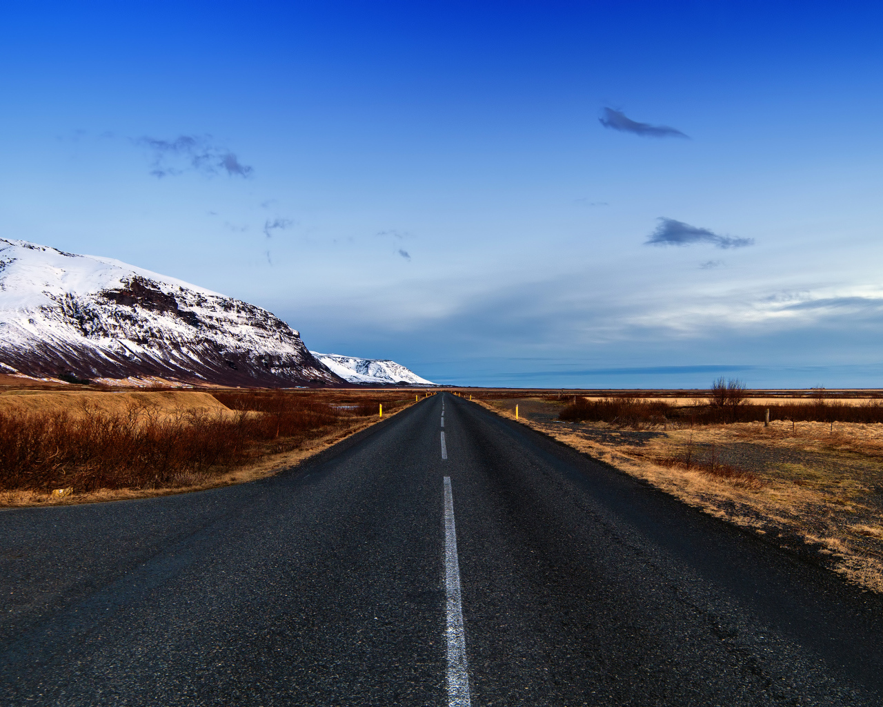 Ровная асфальтовая дорога у заснеженных гор