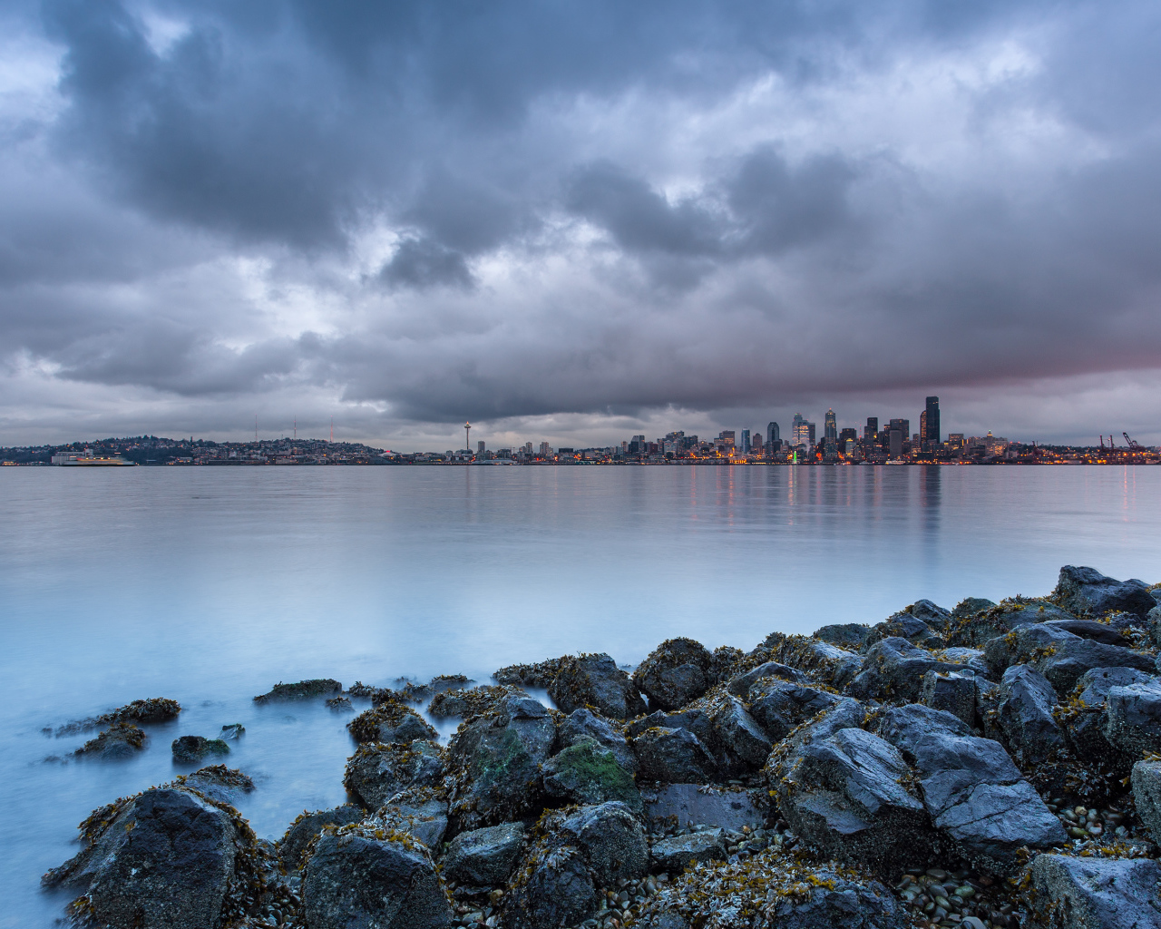 Камни на берегу реки на фоне города под пасмурным небом
