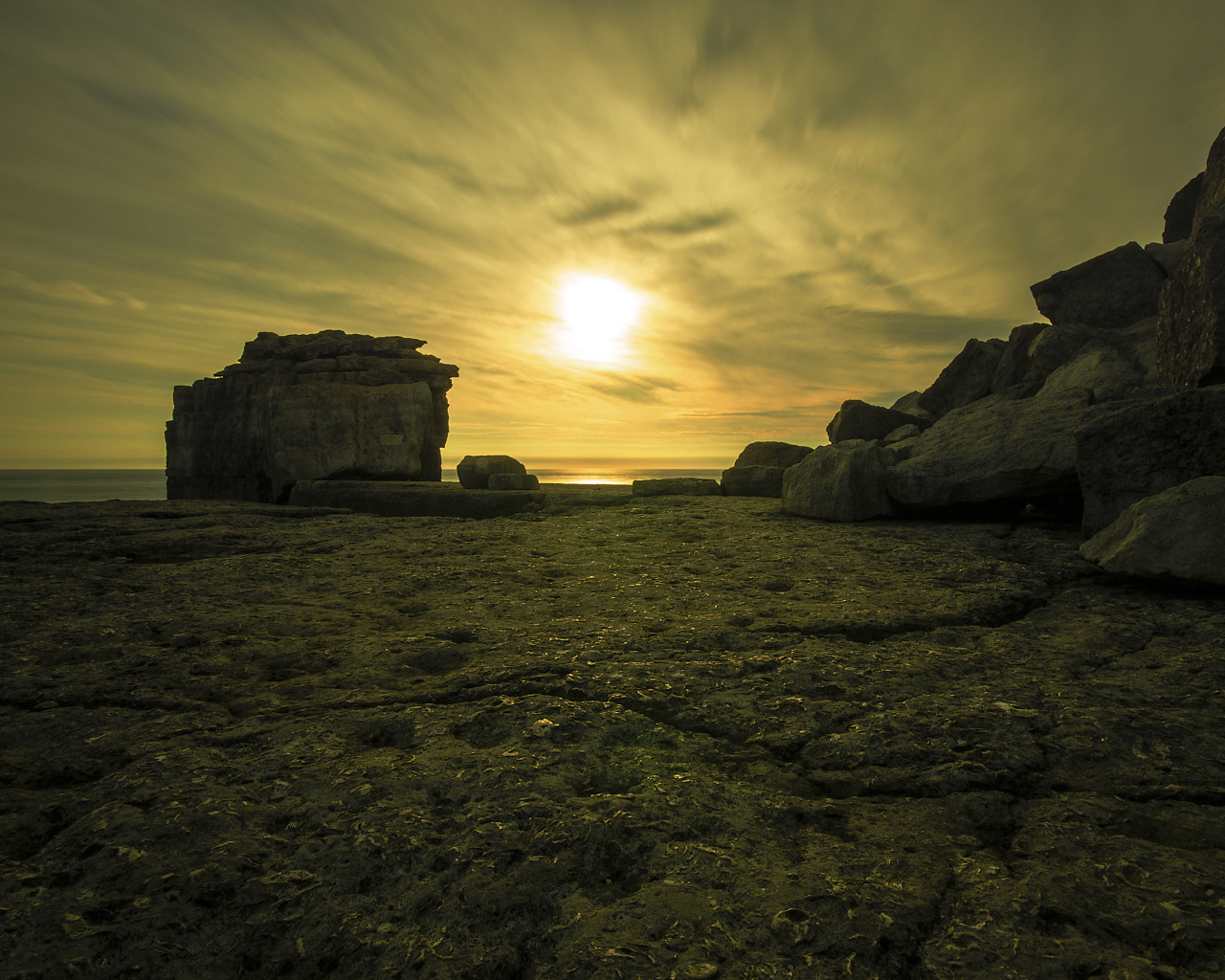 Солнце в облаках освещает камни у моря