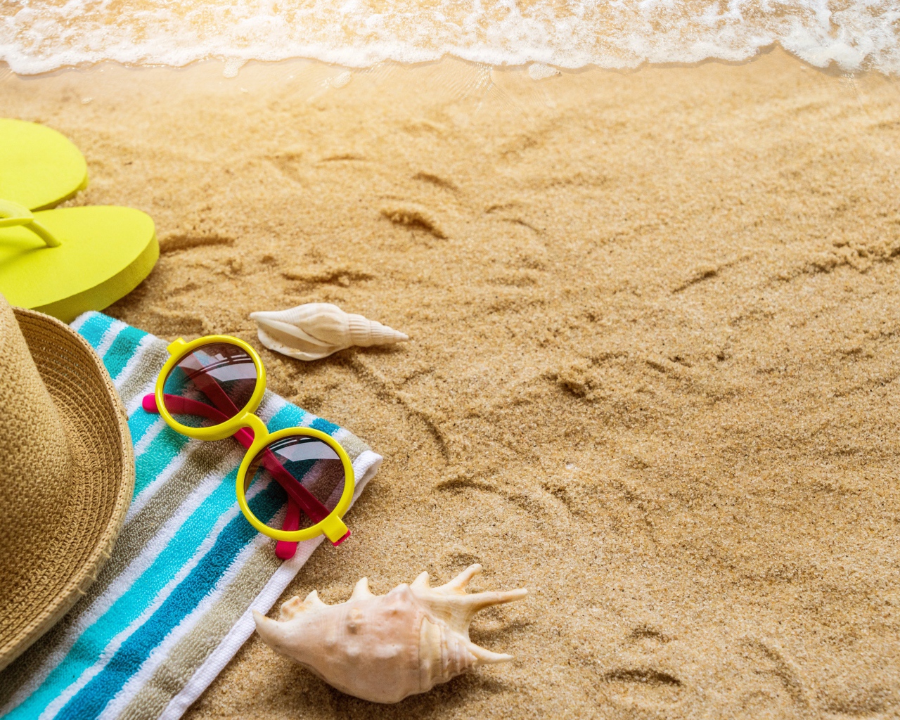 Шляпа, очки, полотенце и ракушки на желтом песке у моря