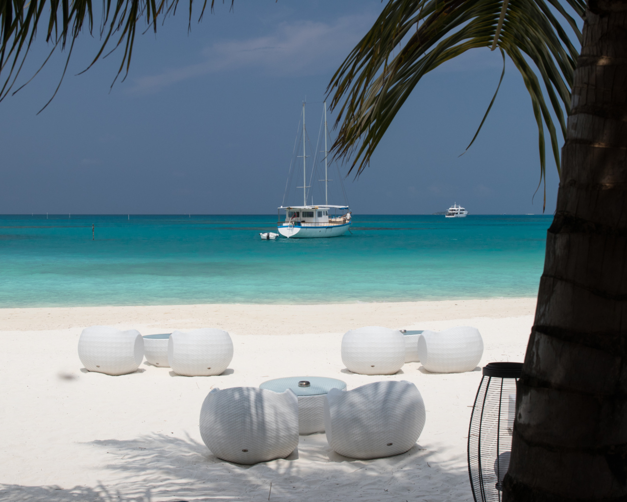 Белые кресла и столики на белом песке на пляже у голубой воды