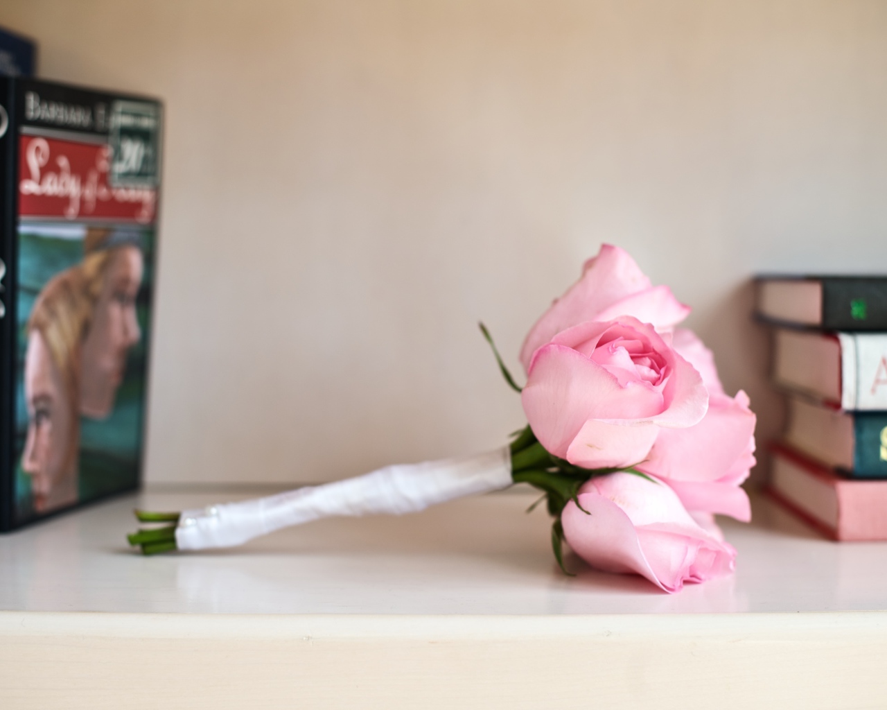 Букет розовых роз лежит на полке с книгами