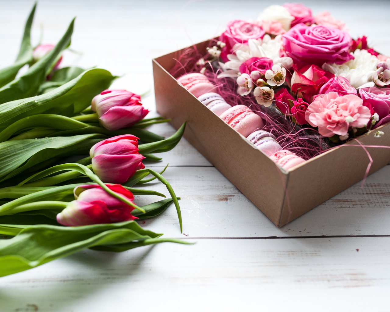 Букет розовых тюльпанов на столе с коробкой печенья макарон и цветами