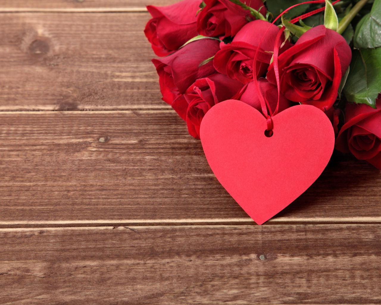 Букет красных роз на деревянном столе с красным сердцем