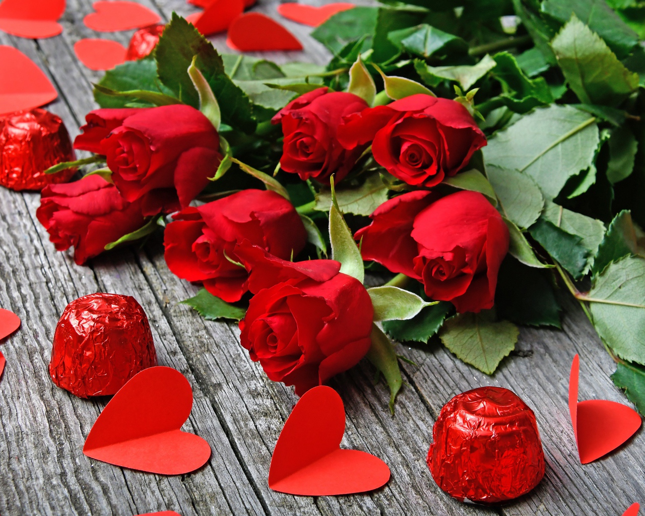 Букет красных роз на деревянном столе с конфетами и красными сердечками