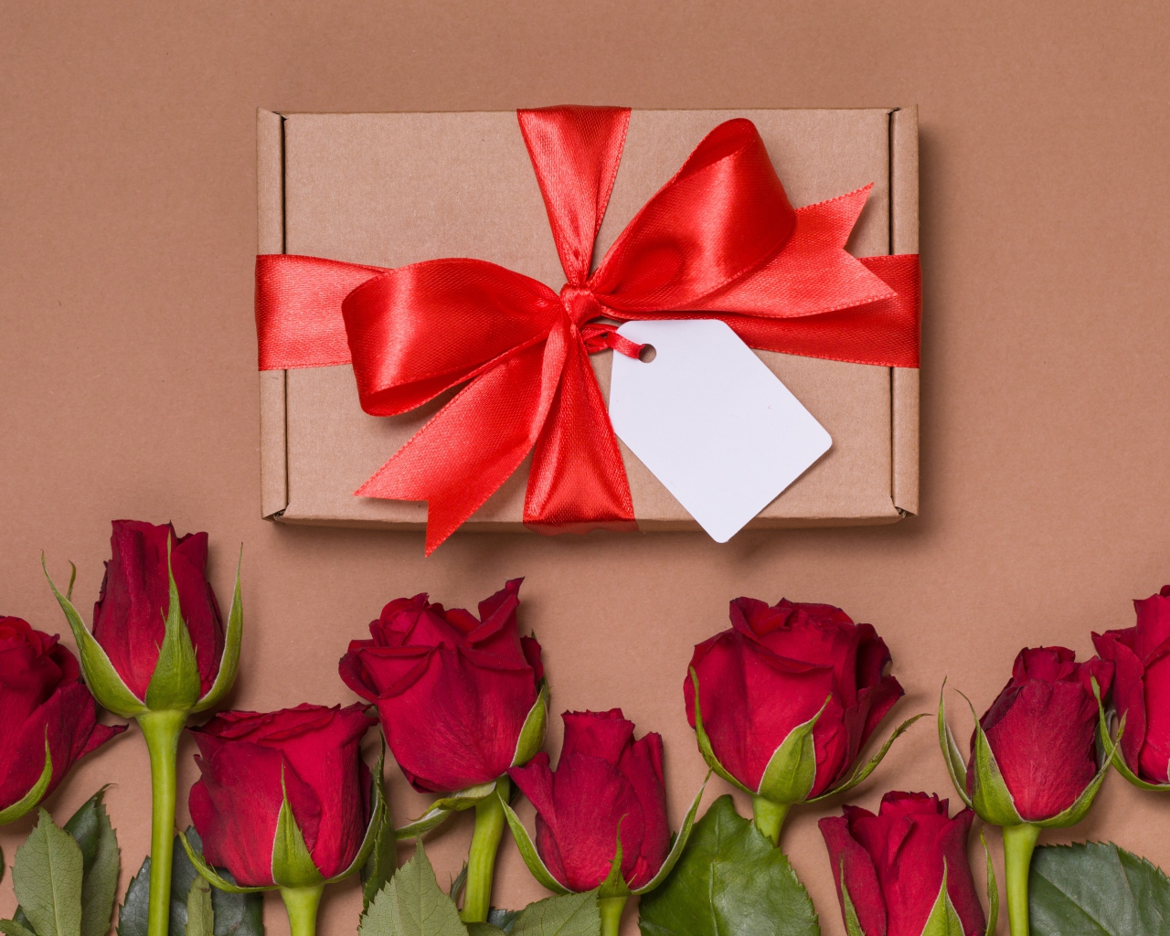 Подарок с красным бантом на бежевом фоне с красными розами