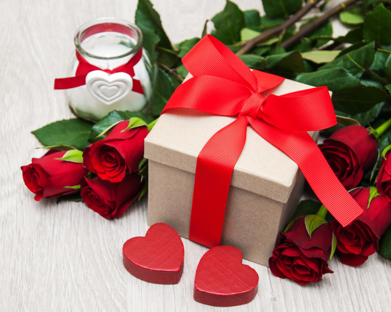 Красивый букет красных роз на столе со свечой и подарком