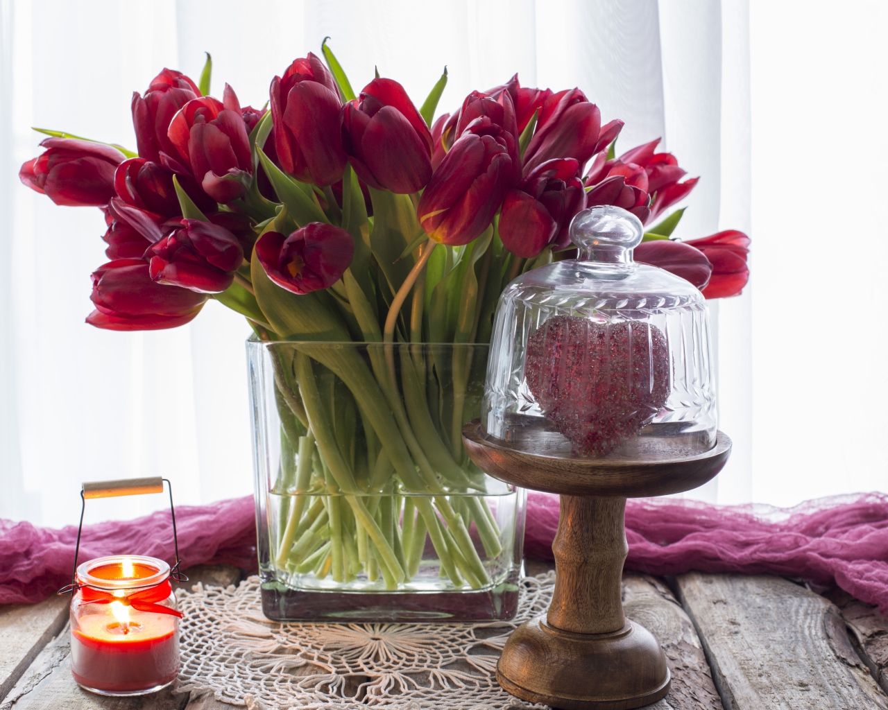 Букет красных тюльпанов в стеклянной вазе на столе со свечой и сердцем 