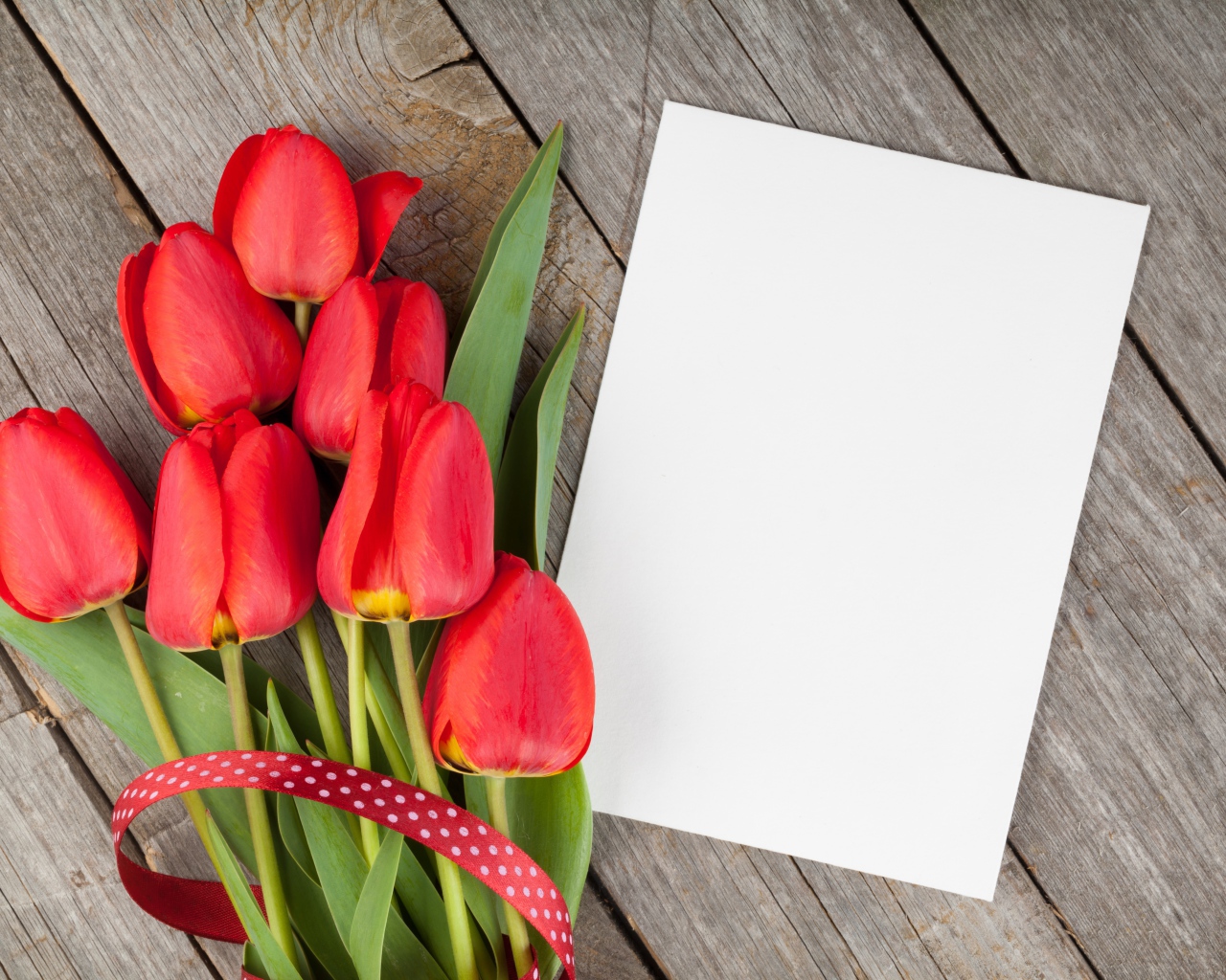 Букет красных тюльпанов с листом бумаги на деревянном столе