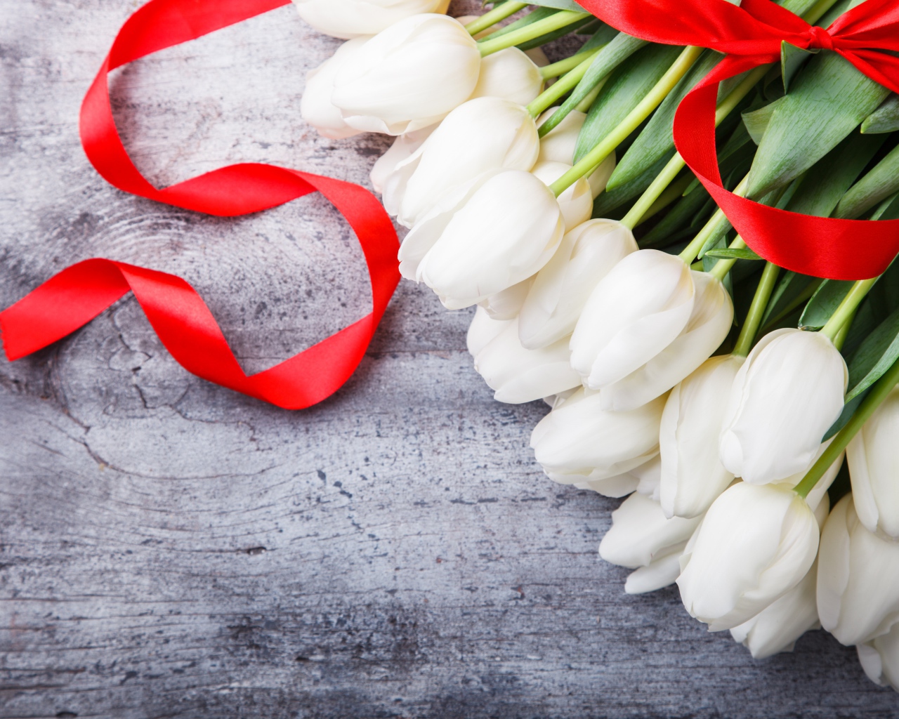 Букет белых тюльпанов с красным бантом на сером столе