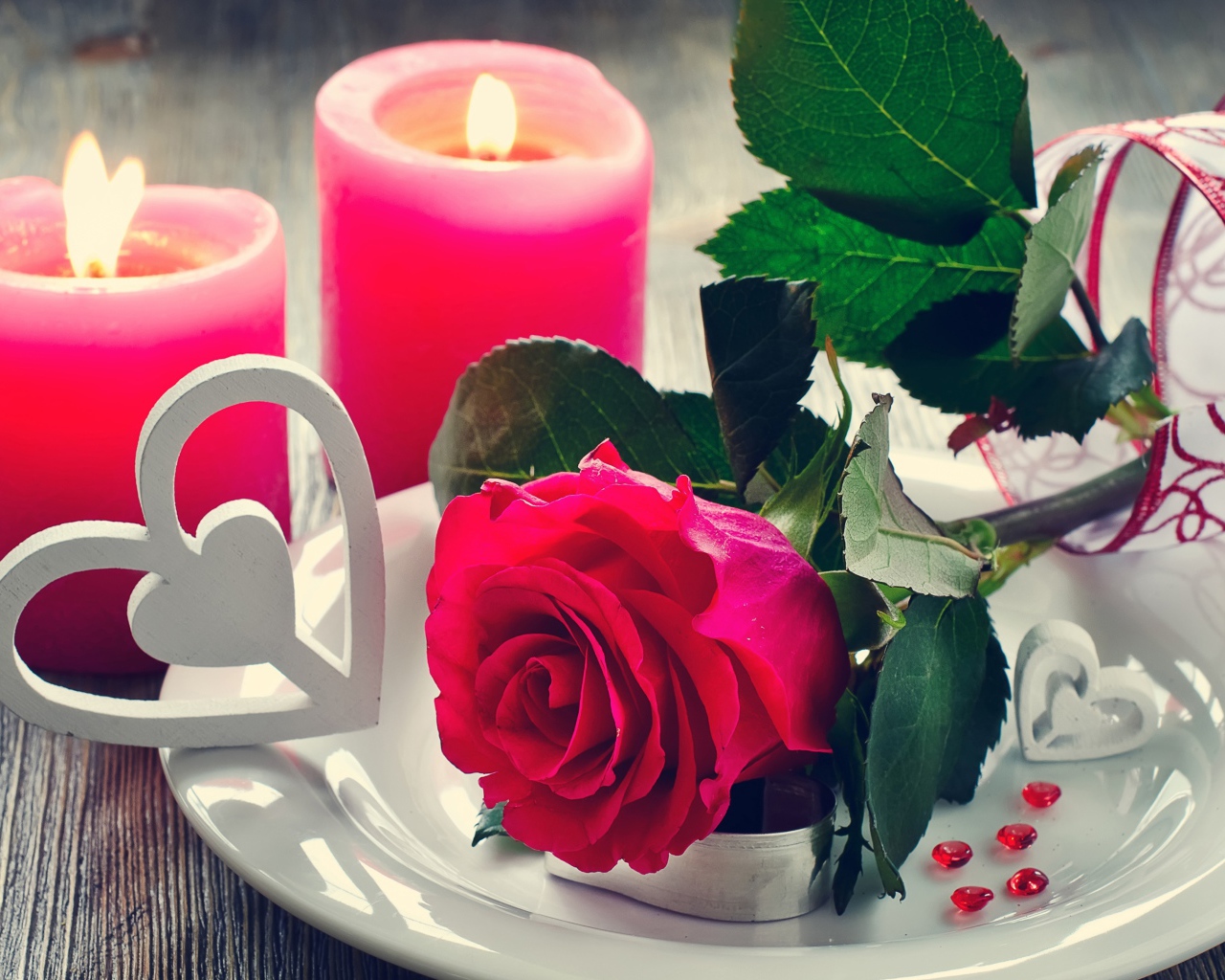 Красная роза на белой тарелке с сердечками на столе с зажженными свечами