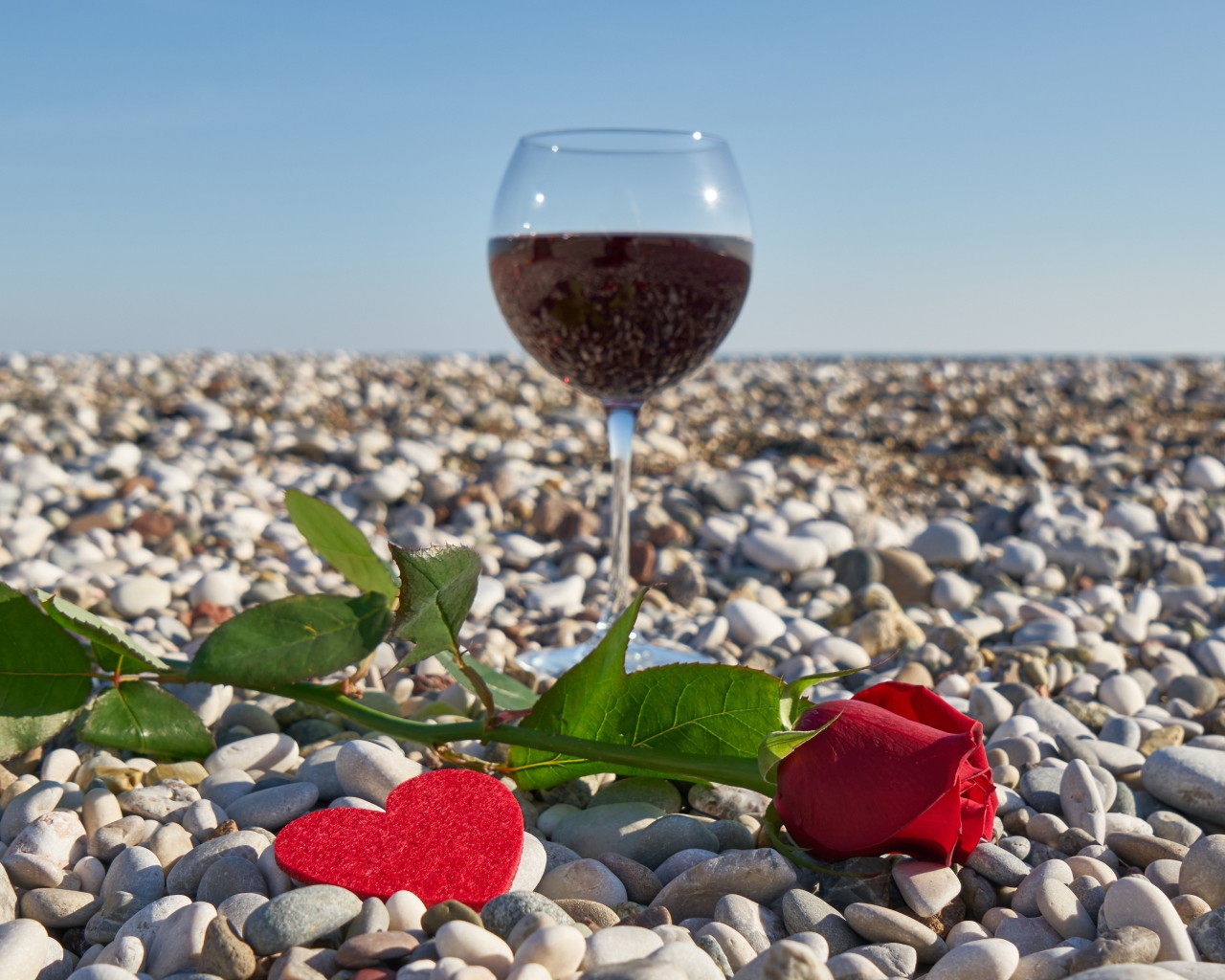 Красная роза на морской гальке с сердечком и бокалом вина