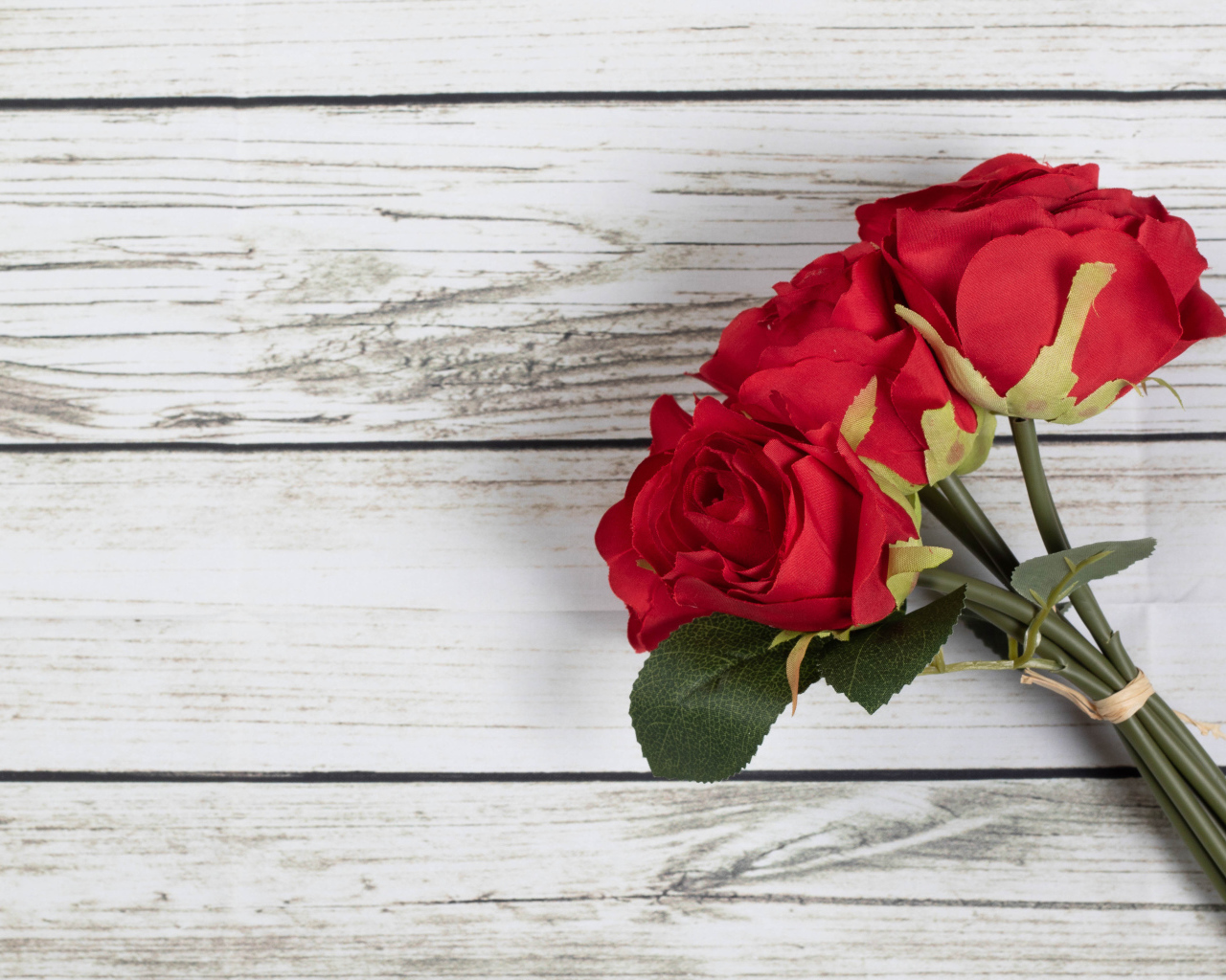 Три искусственные красные розы на деревянном фоне