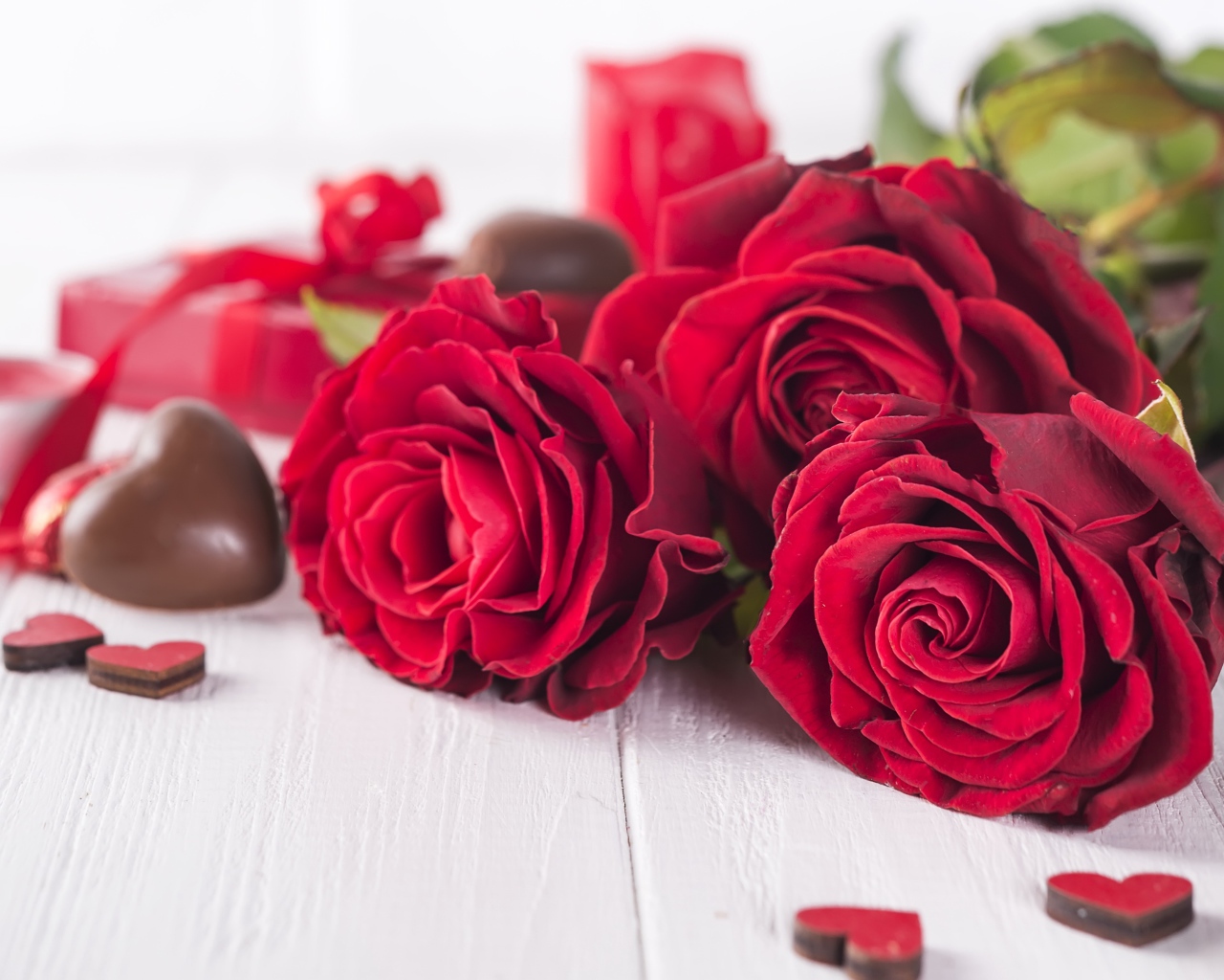Три красивые красные розы на столе с конфетами