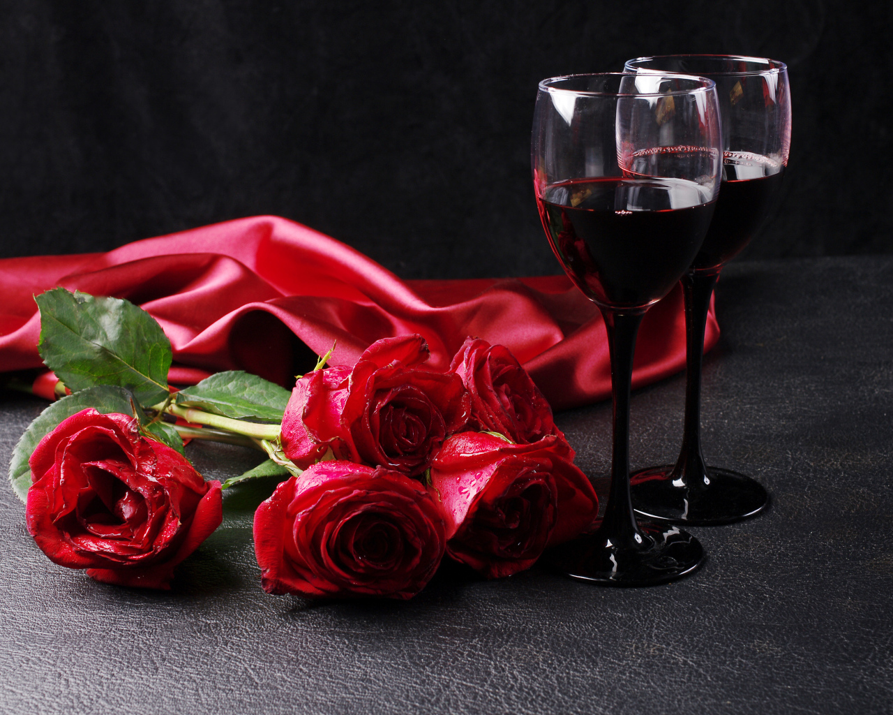 Два бокала с красным вином на черном фоне с букетом красных роз