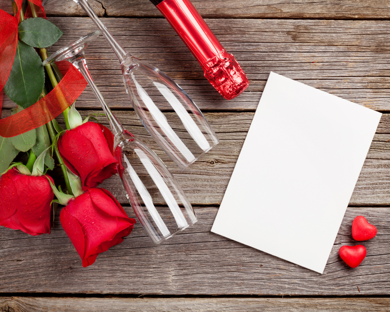 Белый лист бумаги на деревянном столе с бокалами и красными розами