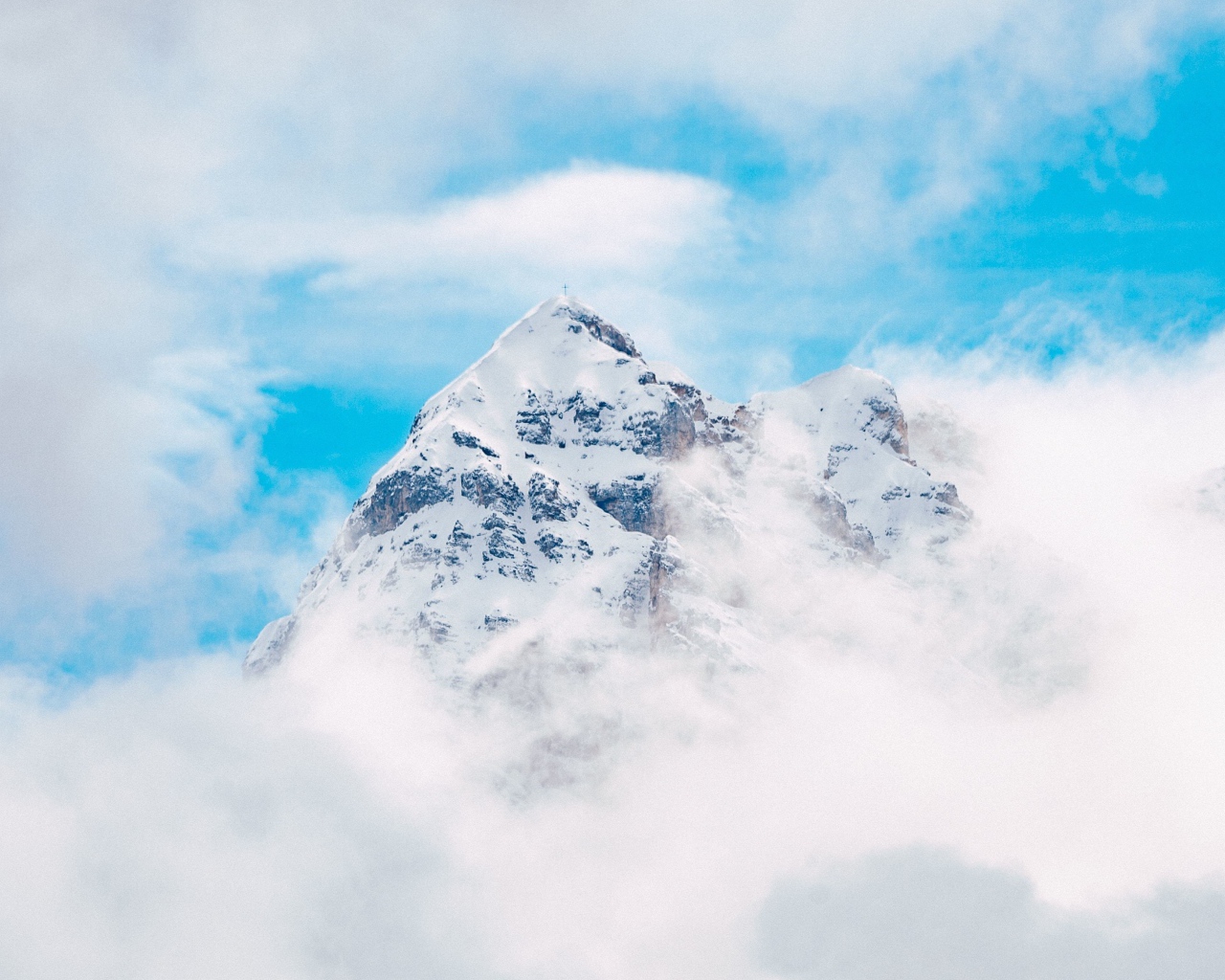 Заснеженная вершина горы в белых облаках под голубым небом