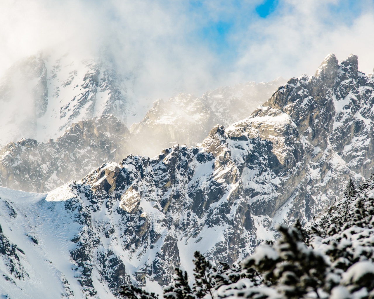 Заснеженные вершины гор под белыми облаками в голубом небе