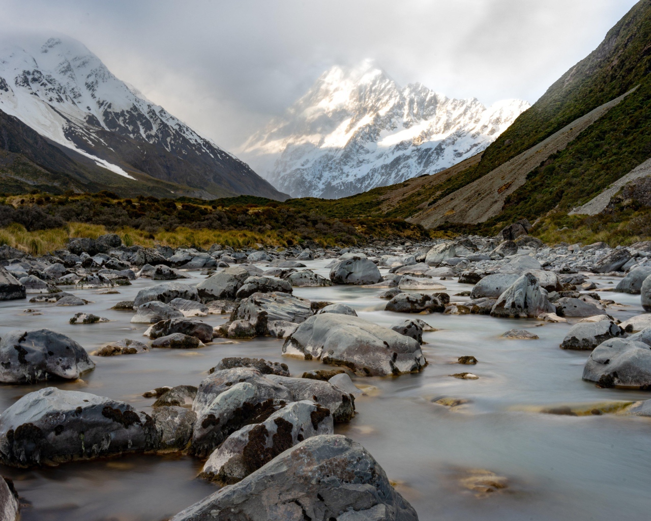 Камни в воде у заснеженных гор 