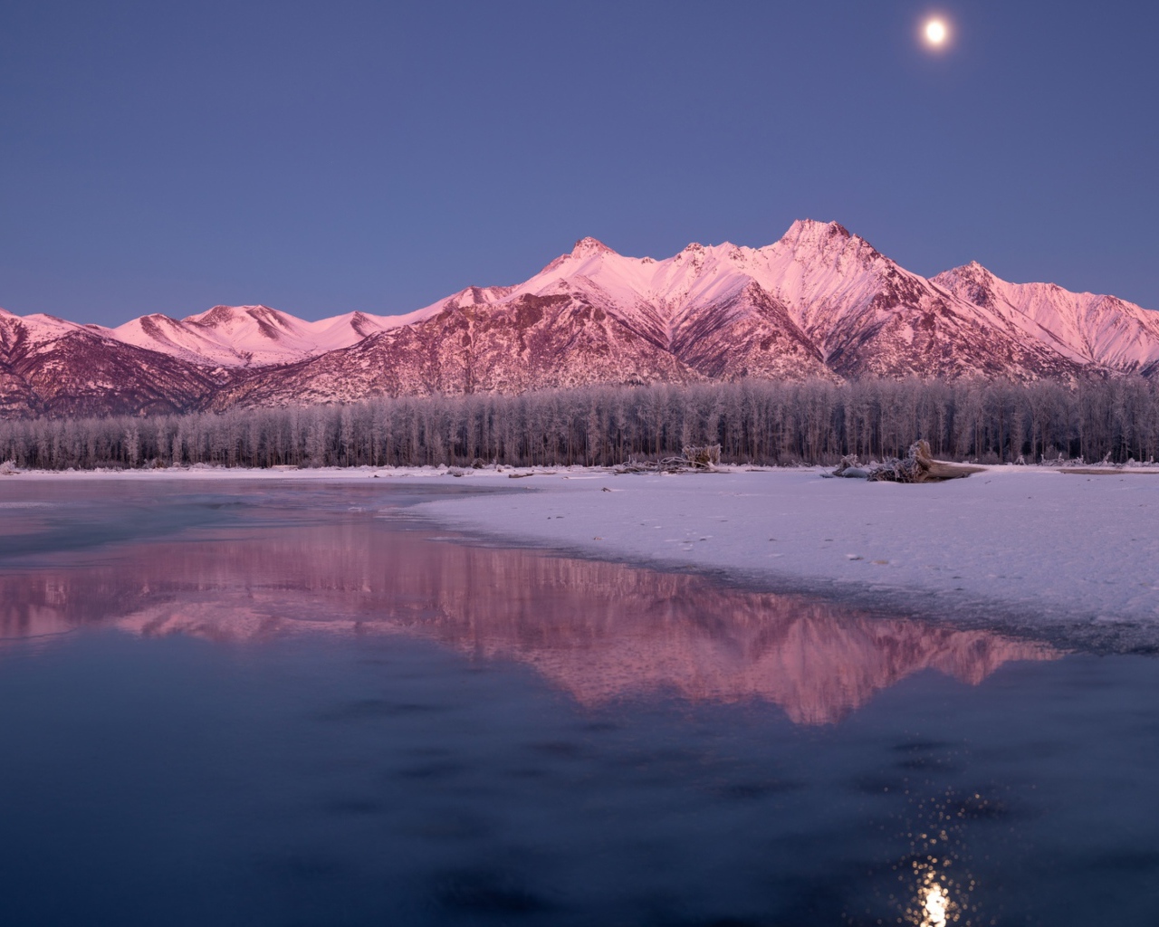 Луна над заснеженными горами отражается в заледеневшем озере 