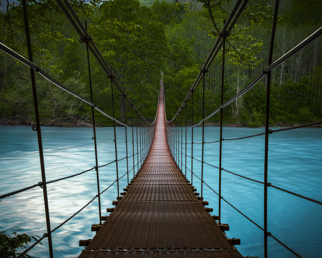 Подвесной мост над быстрой рекой с голубой водой