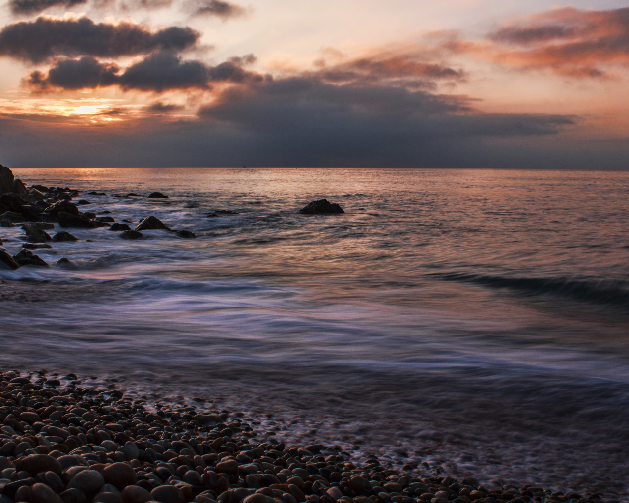 Мелкие камни на берегу моря на закате