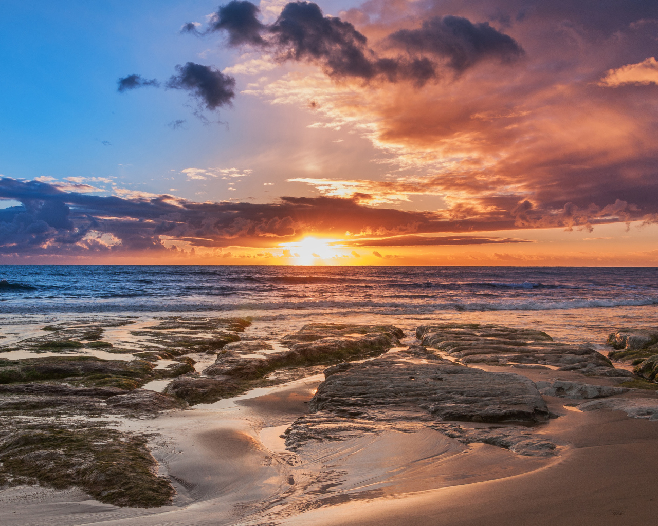 Мокрый песок и камни на берегу океана на закате солнца