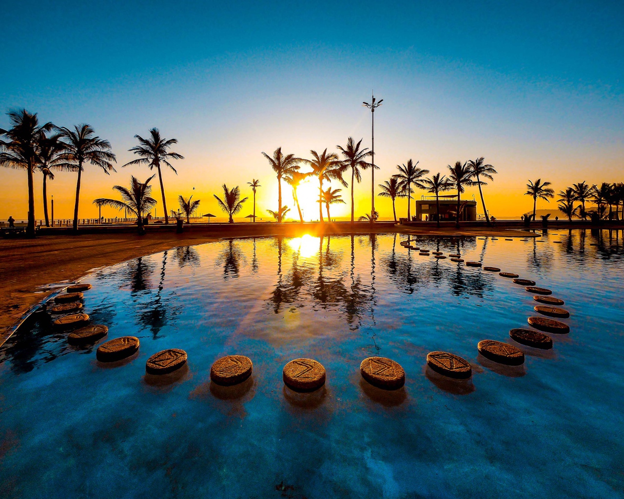 Закат солнца на тропическом пляже на фоне бассейна