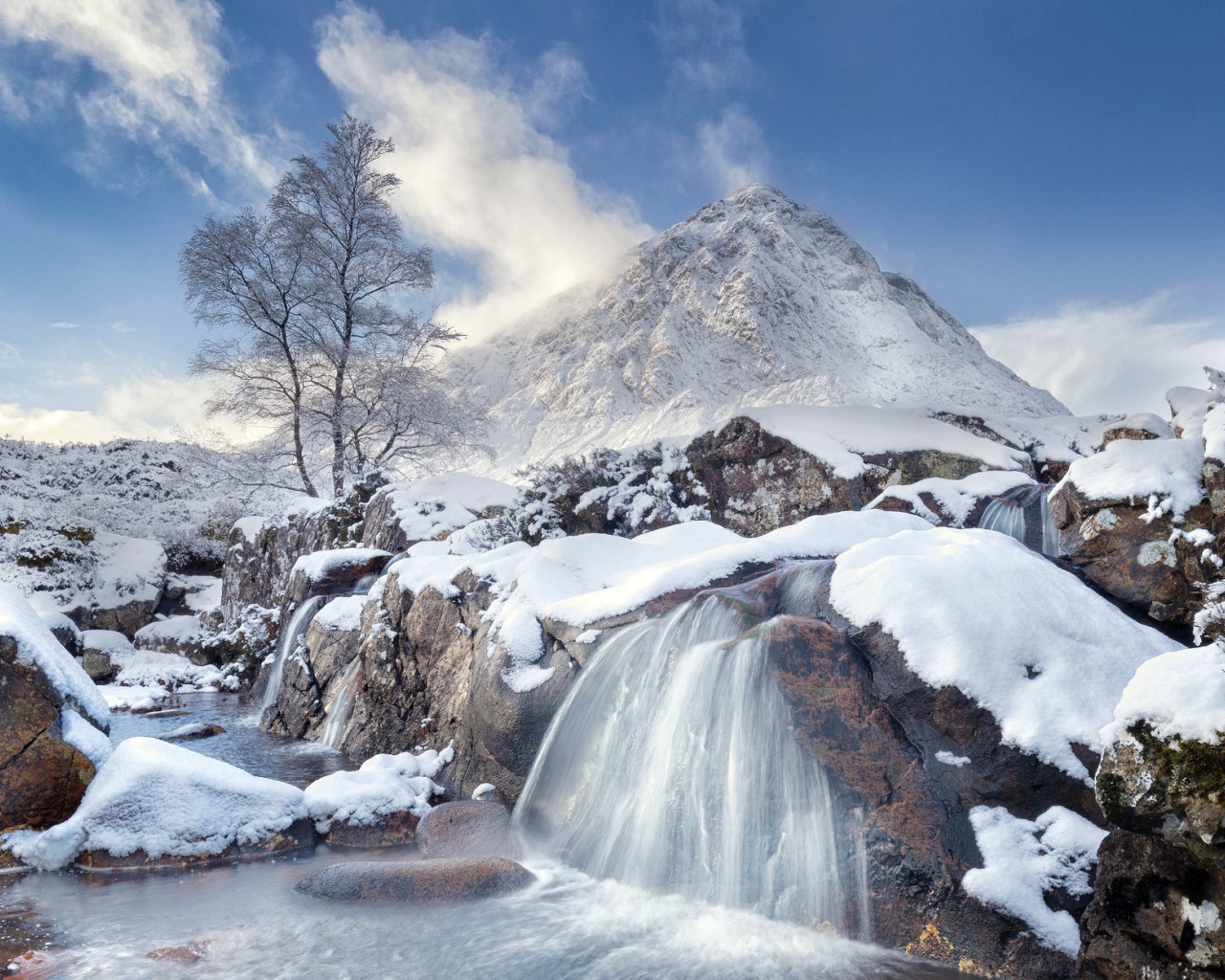 Водопад стекает с камней на фоне заснеженной горы