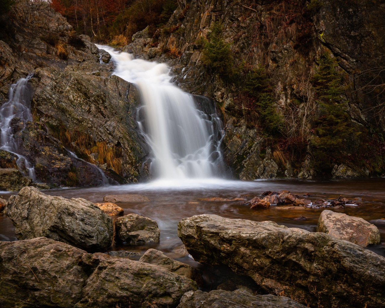 Быстрая вода водопада стекает по камням в горную реку
