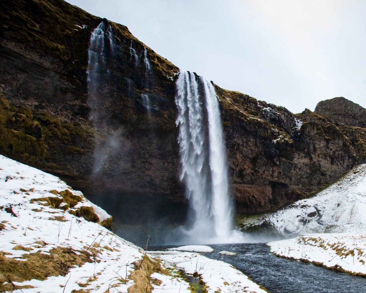 Водопад стекает со скалы в реку с покрытыми снегом берегами