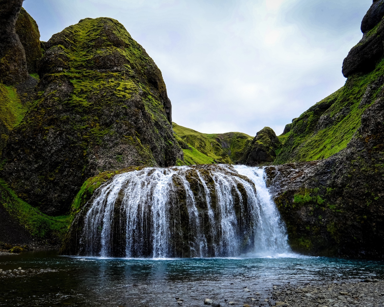 Белая вода водопада стекает по покрытым мхом скалам