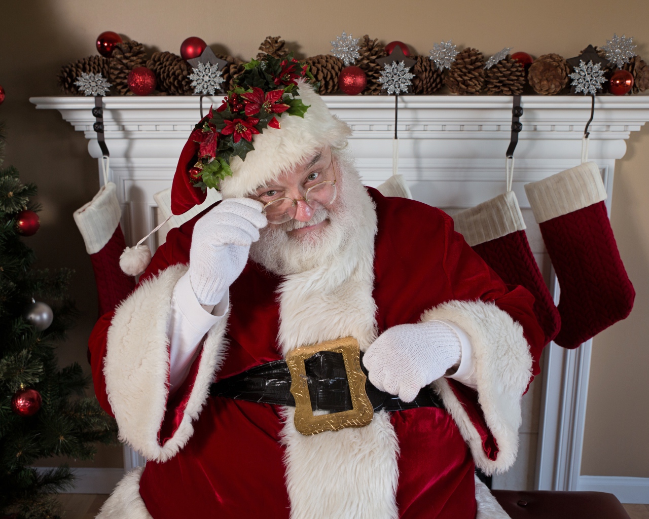 Санта Клаус в очках сидит у камина у новогодней елки