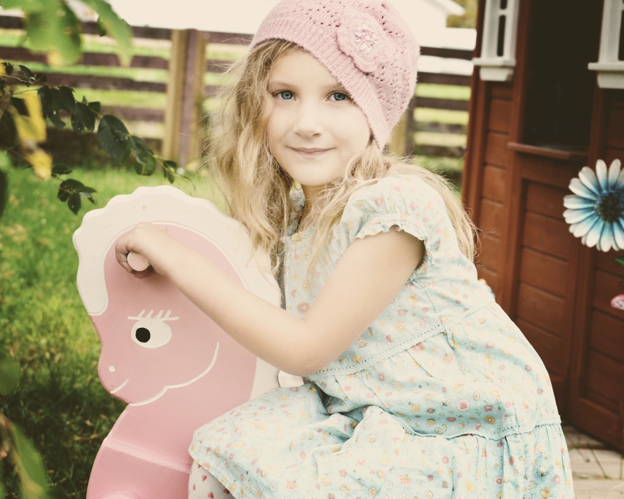 Девочка в платье сидит на деревянной лошади