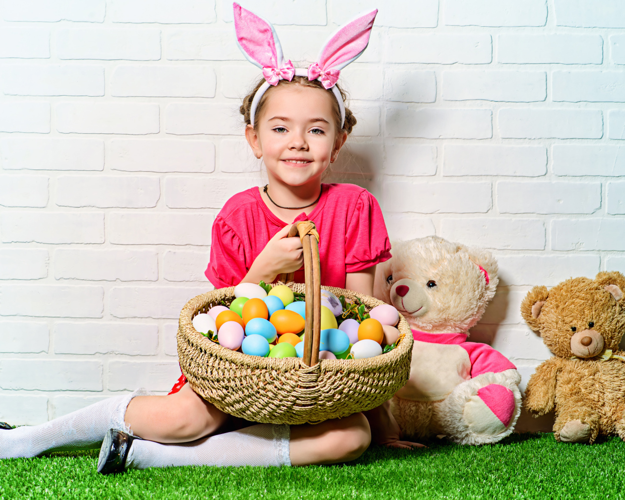 Улыбающаяся девочка сидит у стены с корзиной пасхальных яиц и игрушками