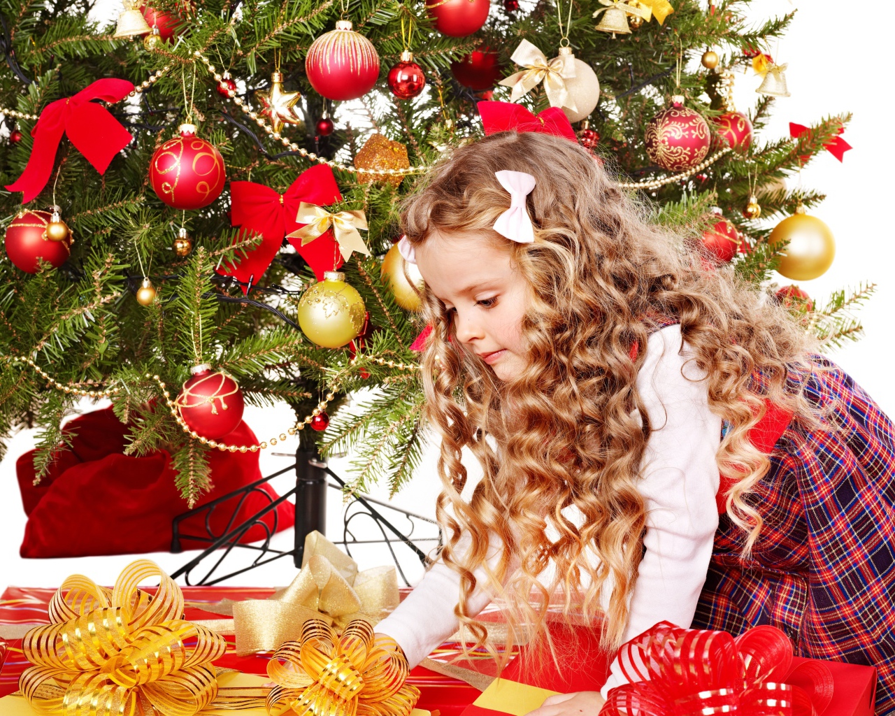 Красивая маленькая девочка смотрит подарки под елкой на новый год 
