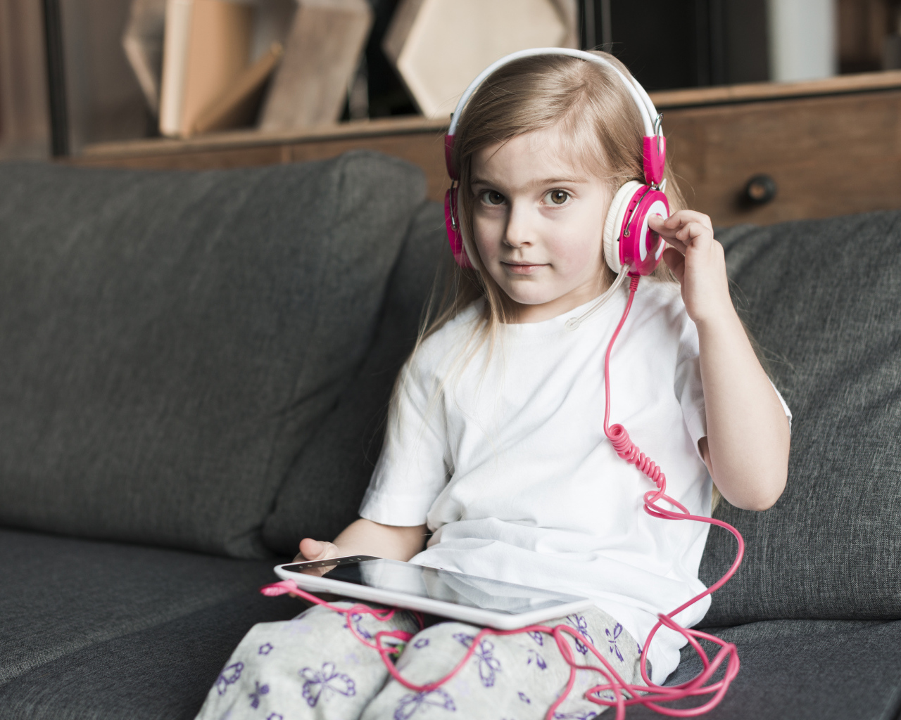 Девочка сидит на диване в наушниках  и с планшетом
