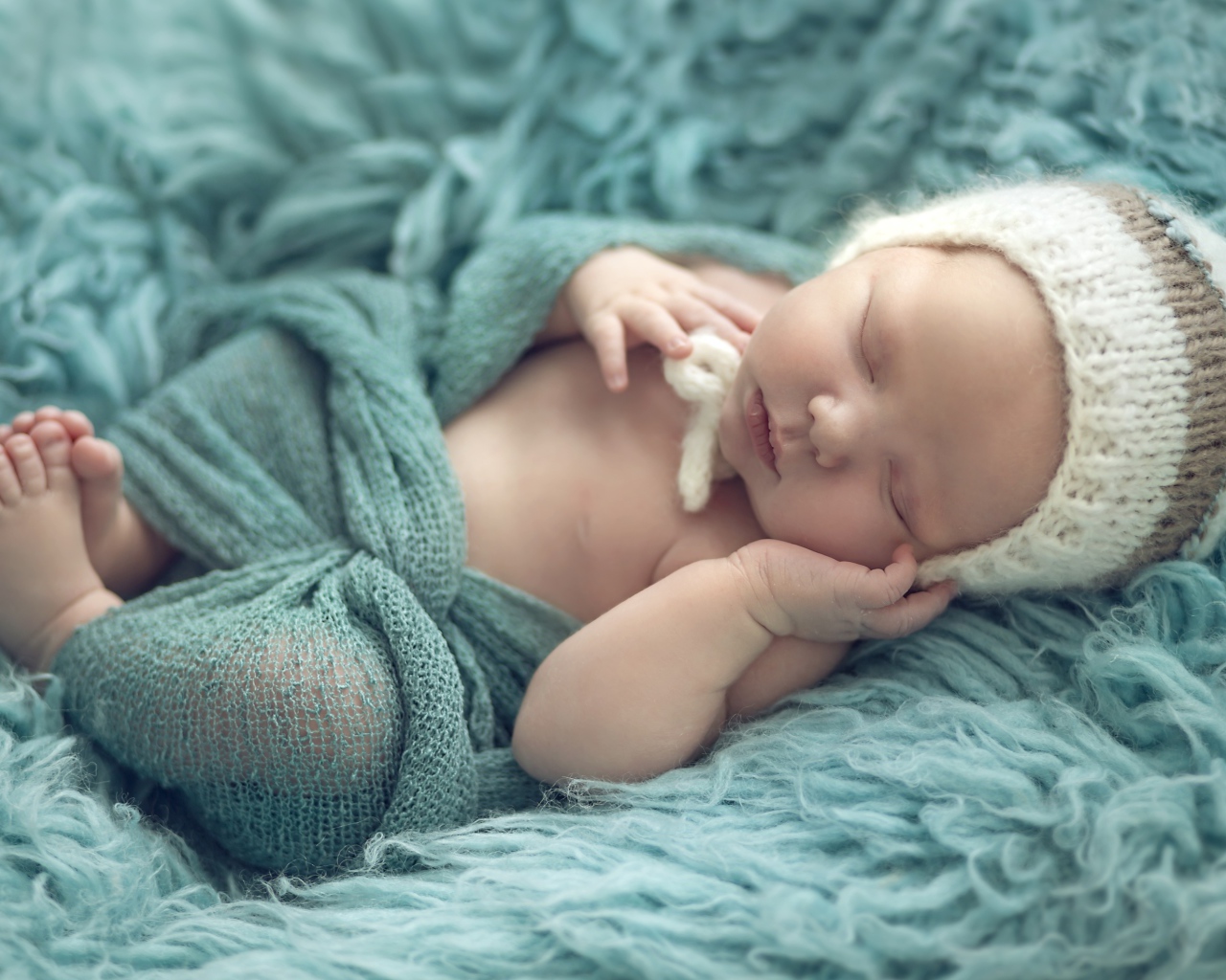 Маленький ребенок в вязаной шапке спит на меховом покрывале