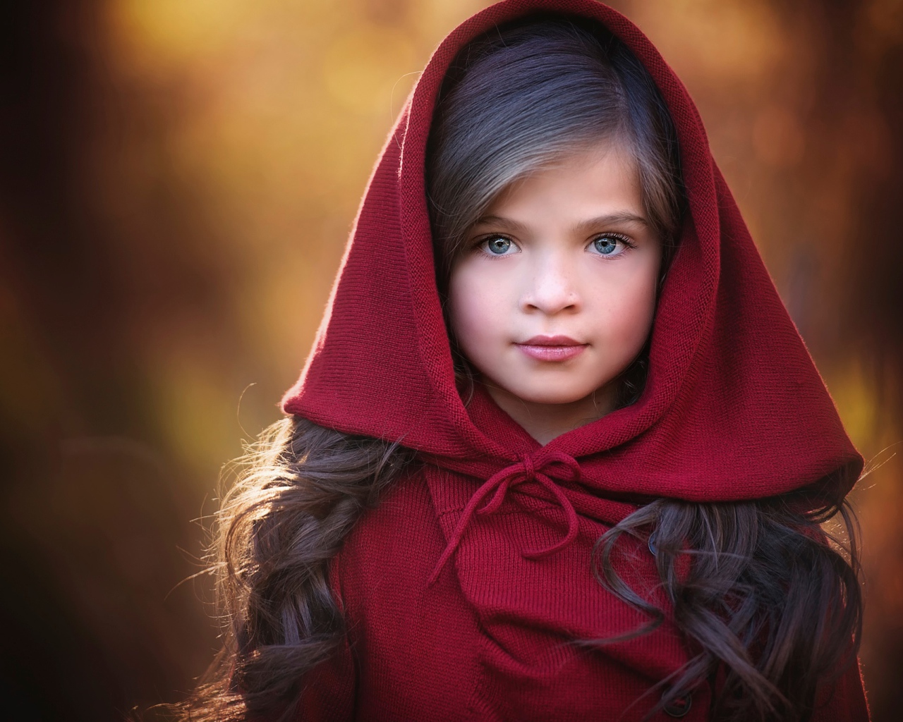Маленькая красивая голубоглазая девочка с красным капюшоном на голове