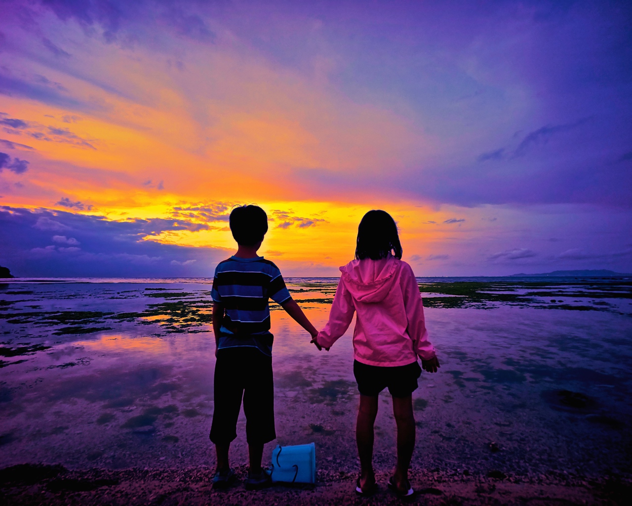 Маленькие мальчик и девочка стоят у воды на фоне заката 