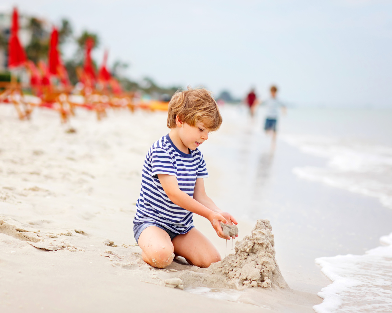 Маленький мальчик строит замок из песка на пляже