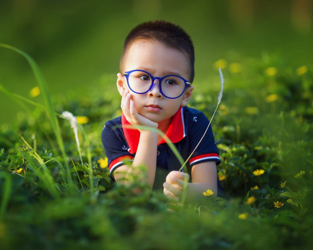 Маленький мальчик в очках лежит на зеленой траве