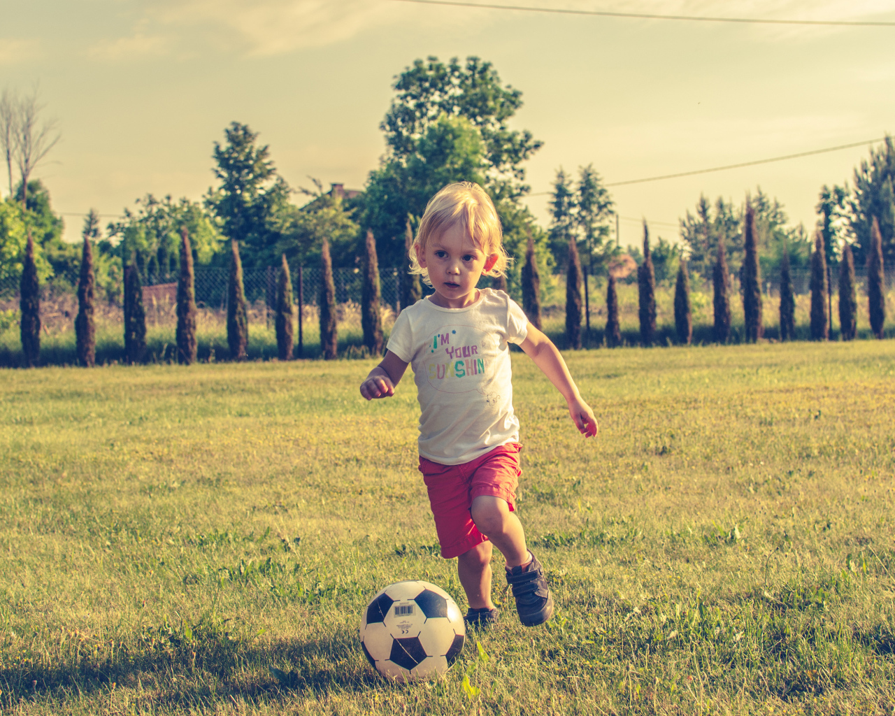 Маленький мальчик играет в футбол на зеленой траве